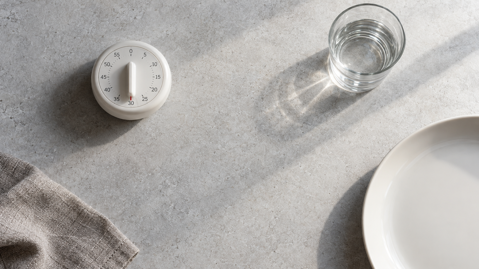 Kitchen timer, small glass of water and empty plate on stone showing the 30-minute morning wait