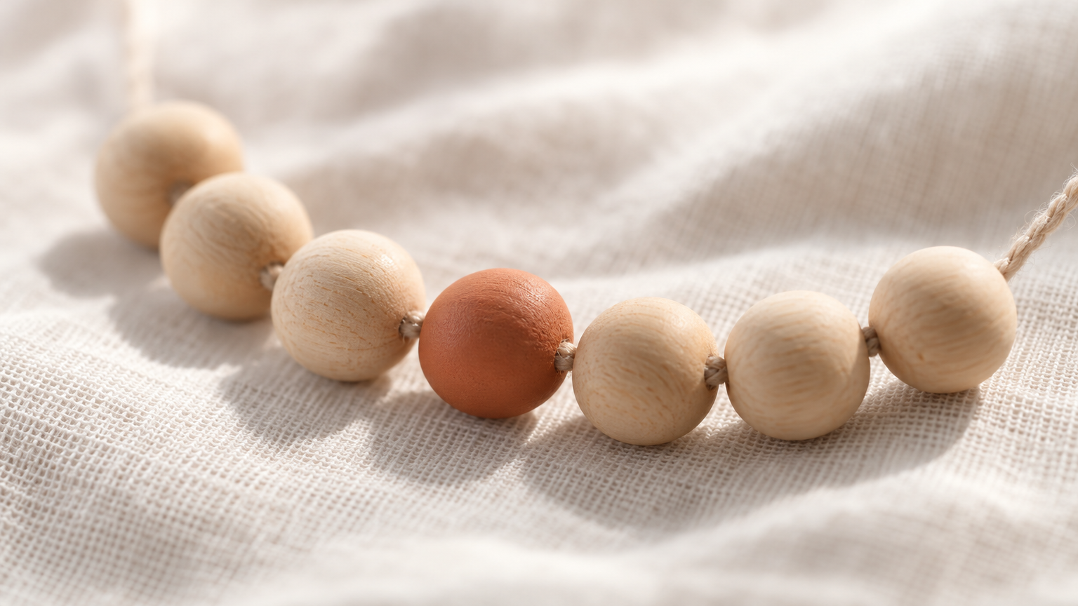 String of seven wooden beads with one terracotta bead on cream linen, representing a once-weekly routine